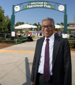 A man poses outside in front of a park.